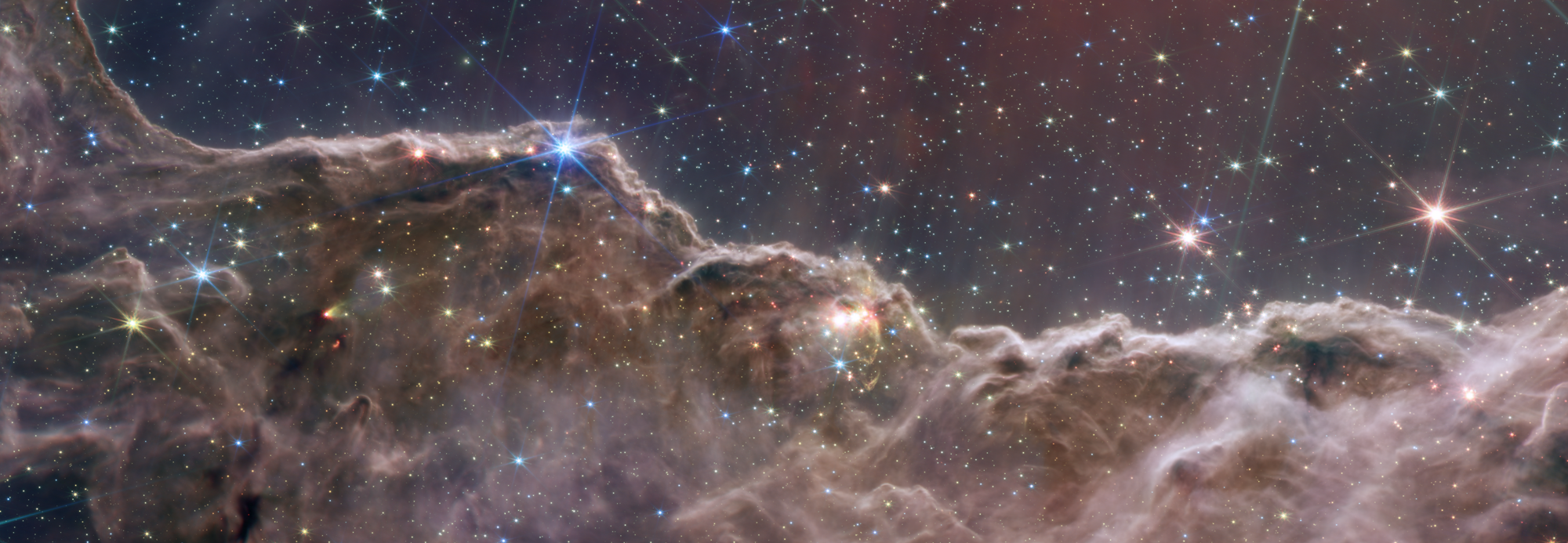 Webb image of the Cosmic Cliffs in the Carina Nebula showing undulating orange-green cloudscape under a starfield